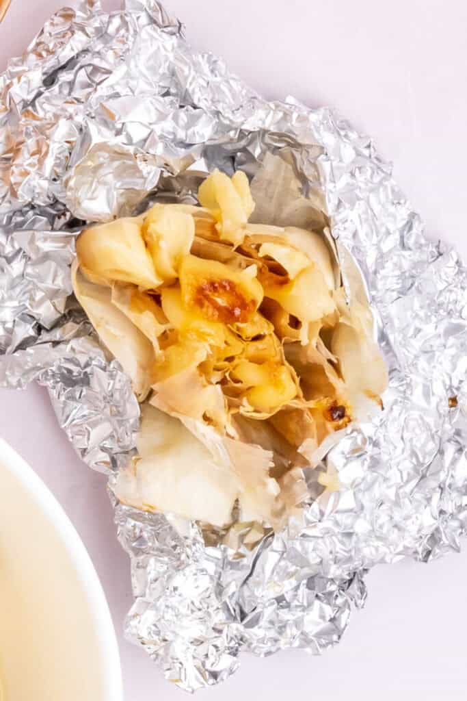 Preheat your air fryer to 390°F (200°C). Cut off the top of the head of garlic and drizzle it with olive oil (1 teaspoon). Wrap it tightly in aluminum foil. Place the wrapped garlic directly in the air fryer basket and cook for 25 minutes or until the cloves are soft when pressed and lightly golden brown.