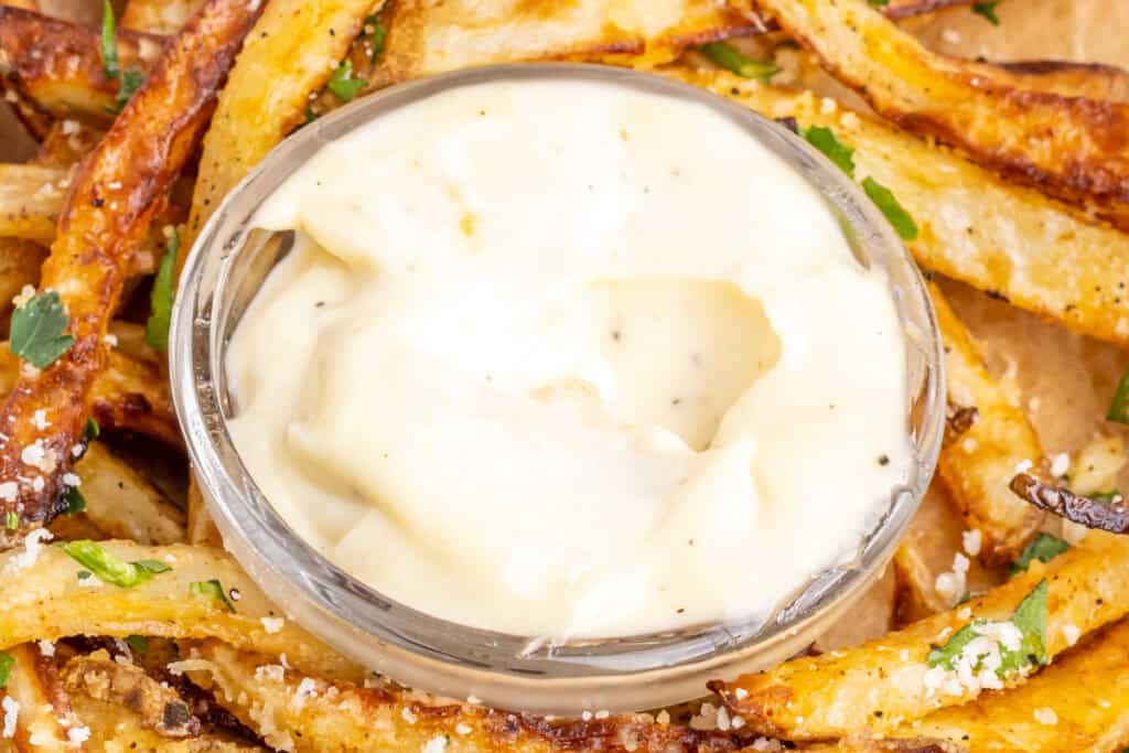 garlic aioli in small glass bowl surrounded by fries
