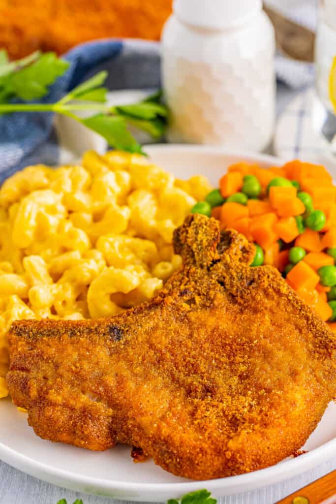 shake and bake pork chop on plate with mac and cheese and peas and carrots