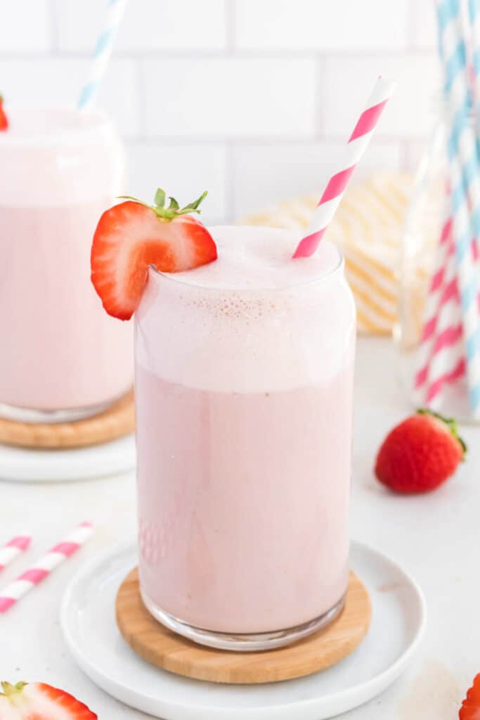 glass of strawberry milk on a coaster with a pink and white straw