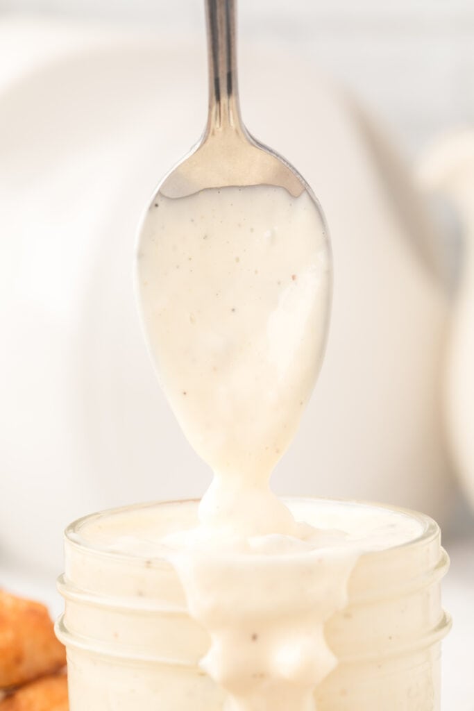 closeup of tartar sauce dripping off a spoon over a glass jar filled with sauce
