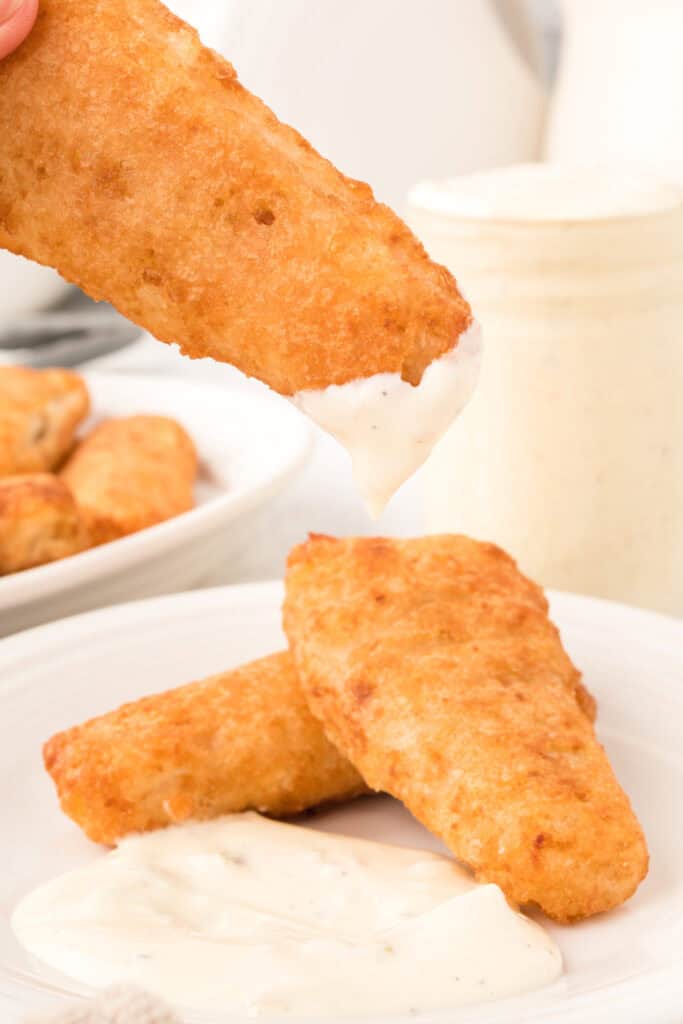 fried fish portions being dipped into tartar sauce