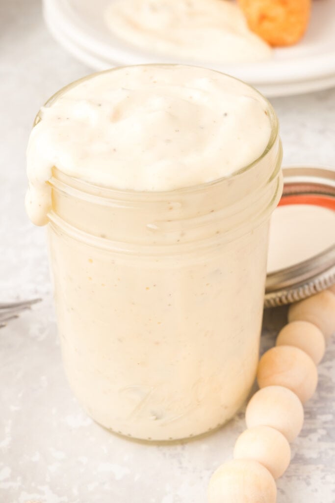 up close of tartar sauce in mason jar with lid off behind it