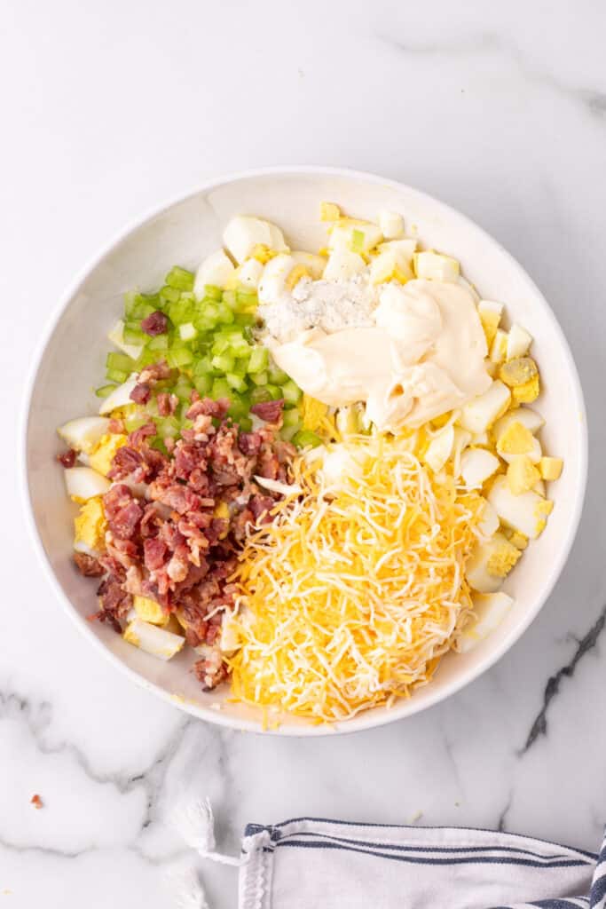 ingredients for cheddar bacon ranch egg salad in bowl before being mixed