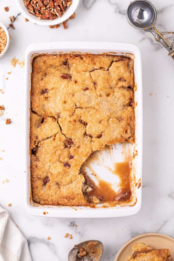 pecan pie cobbler in baking dish with scoop taken out of the cobbler