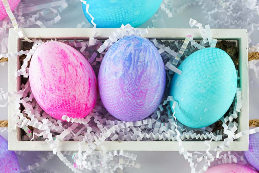 three different colors of fabric textured eggs in wooden box