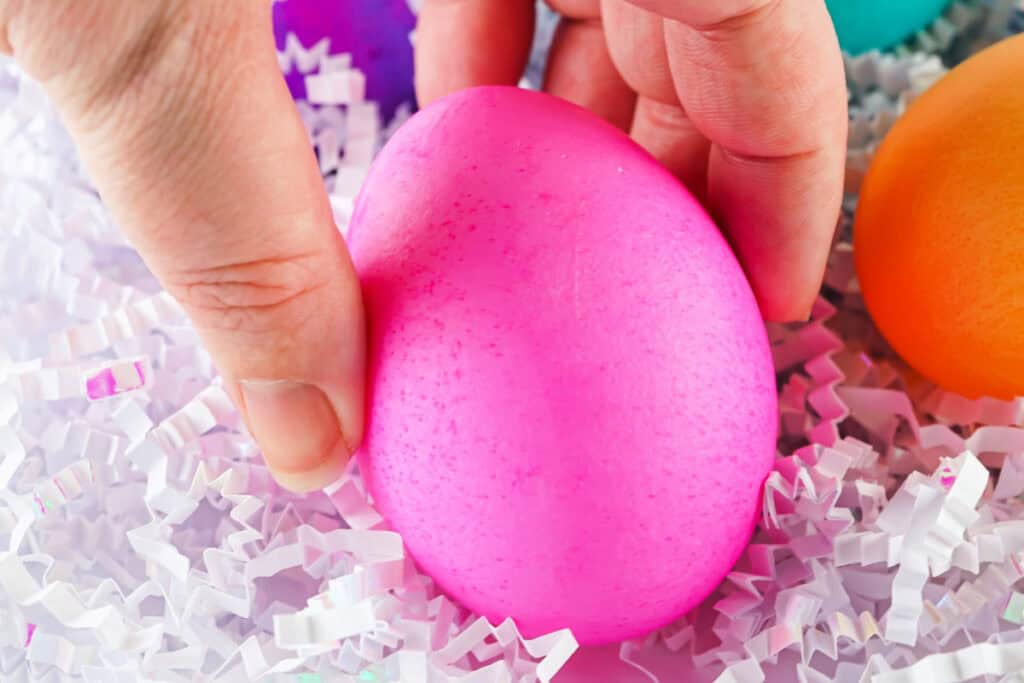 hand holding a pink food coloring dyed easter egg