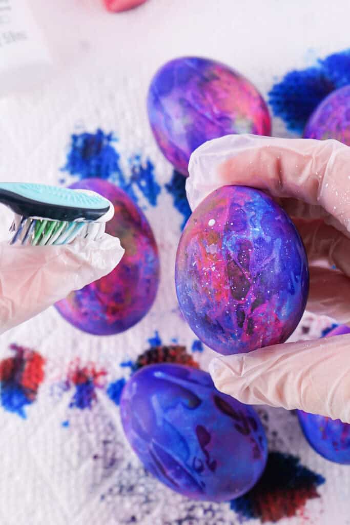 a toothbrush flicking white paint onto a dyed egg