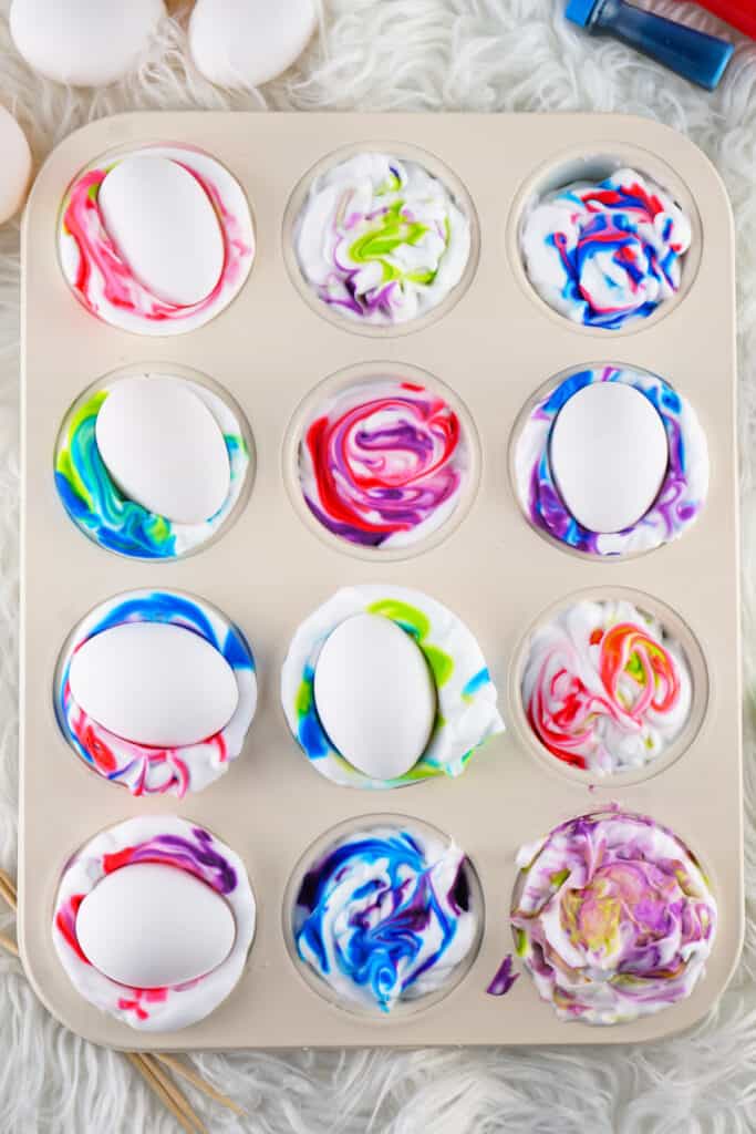 eggs placed on top of the colored shaving cream in the muffin tin