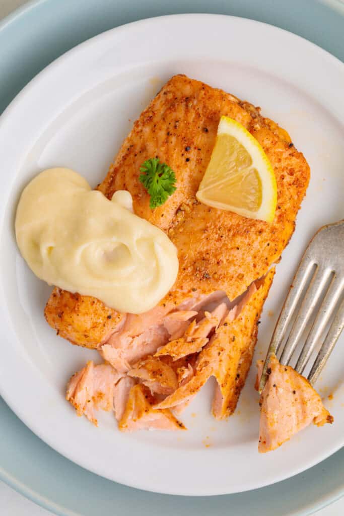 piece of air fryer frozen salmon after being cooked topped with lemon butter sauce, parsley sprig, and lemon