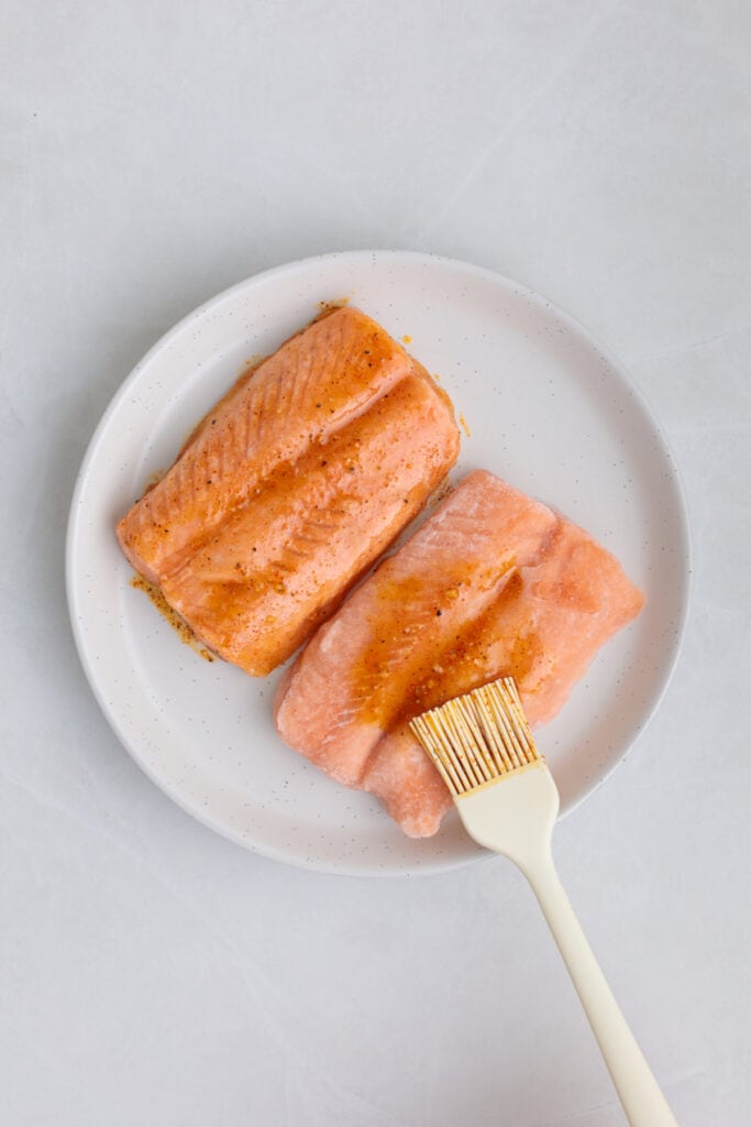 two pieces of salmon on plate being brushed with the seasoning mix