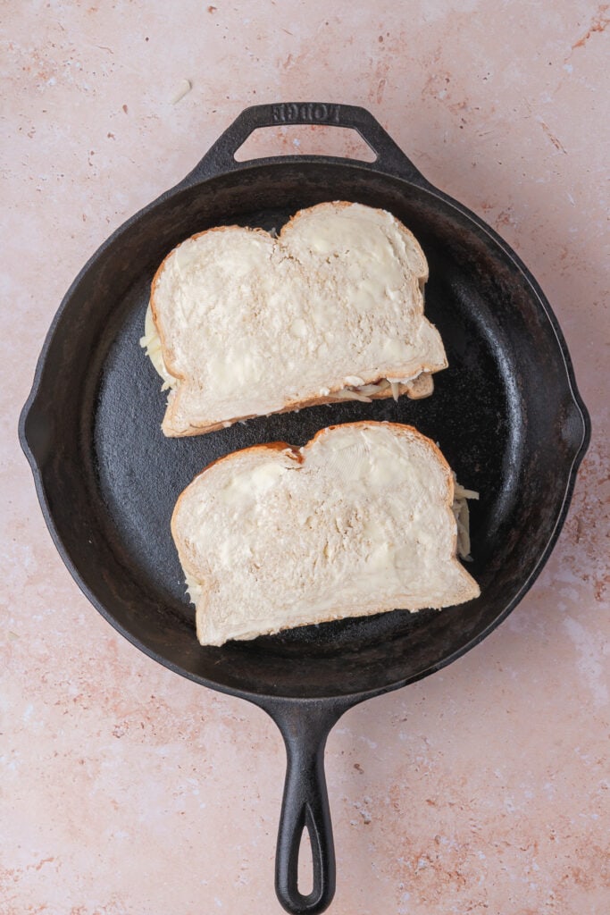 Two buttered sandwiches placed in a cast iron skillet, ready for grilling