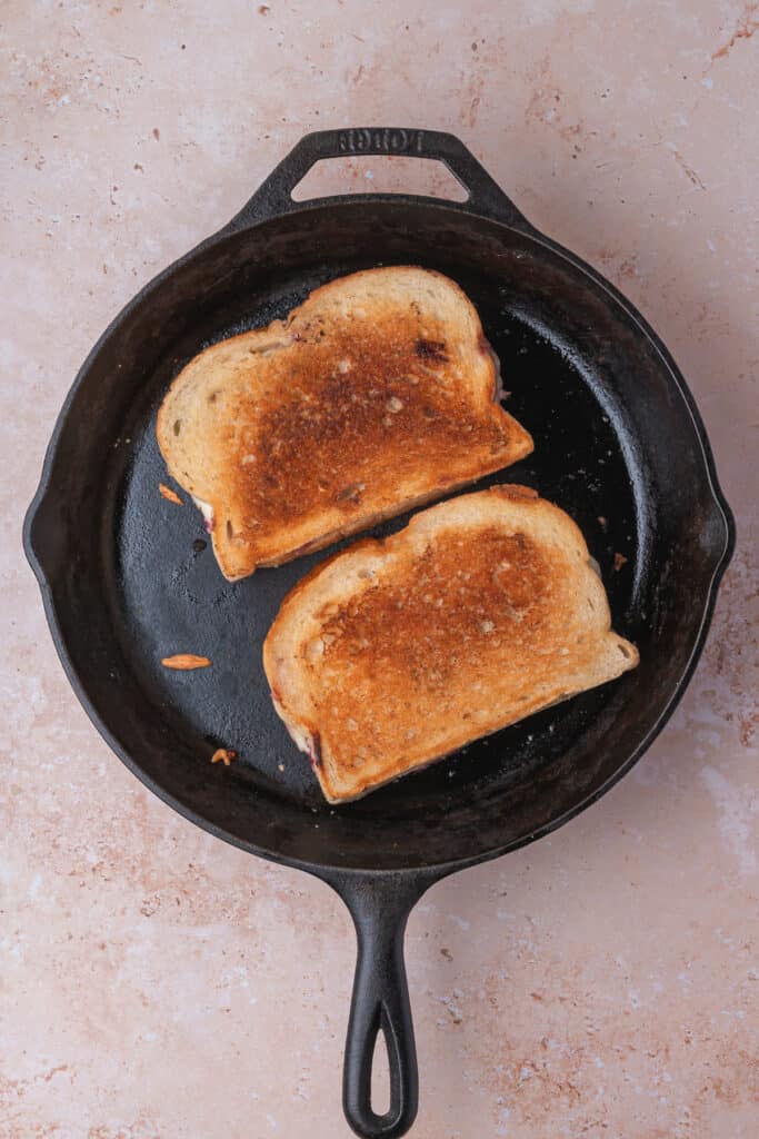 Two golden brown grilled cheese sandwiches cooking in a cast iron skillet
