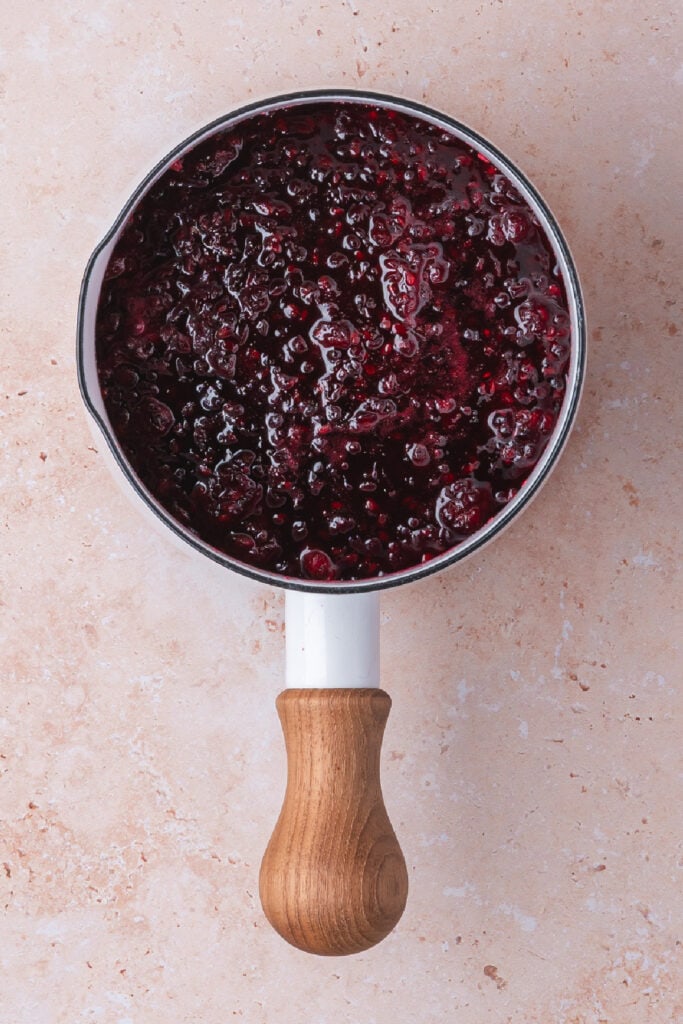 Simmered blackberry jam in a white saucepan with a wooden handle, thick and glossy
