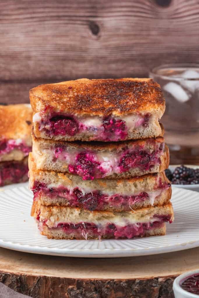 Tower of four blackberry grilled cheese sandwich halves stacked on a white plate