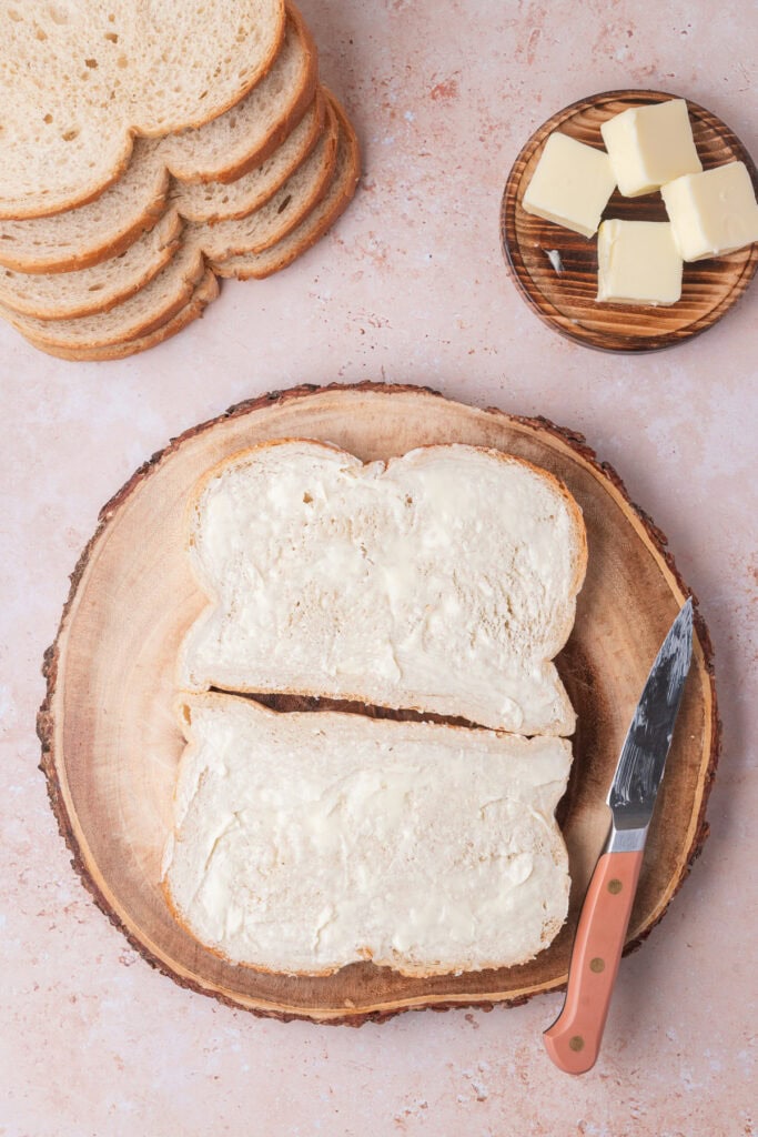 Sourdough slices spread with butter, stacked beside a wooden plate with butter cubes