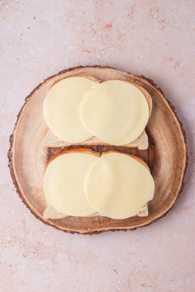 Slices of provolone cheese placed on top of sourdough bread on a wooden cutting board