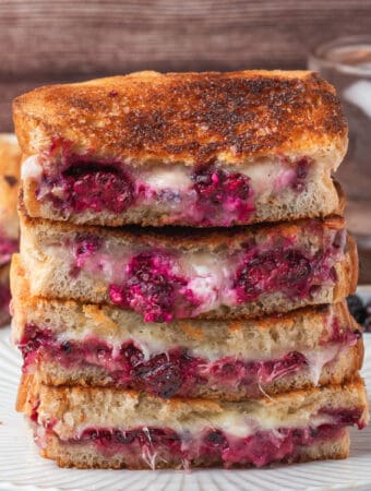 Square image showing a close-up stack of grilled cheese sandwiches filled with melted cheese and blackberries