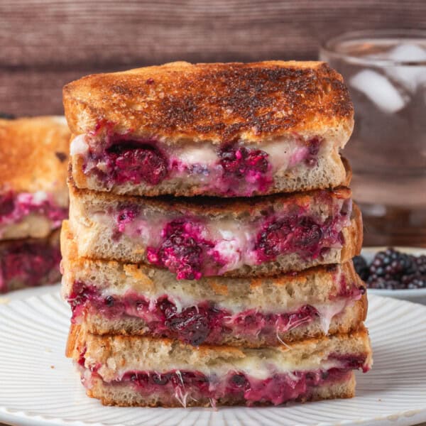 Square image showing a close-up stack of grilled cheese sandwiches filled with melted cheese and blackberries