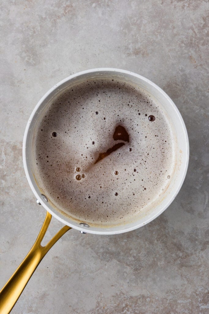 Brown butter in a saucepan with golden bits and foam, showing the correct color and texture.