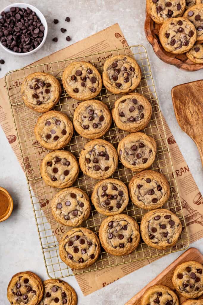 Cooling rack filled with golden brown chocolate chip cookies, surrounded by scattered chips.