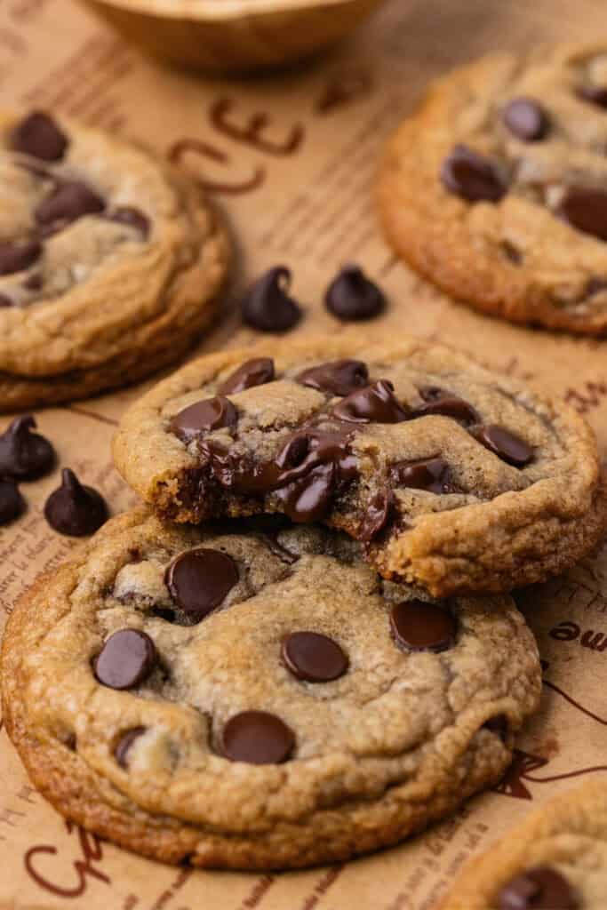 Chocolate chip cookies on brown parchment, one cookie with a bite showing gooey center.