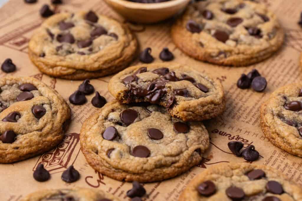Wide view of chocolate chip cookies on parchment paper, surrounded by chocolate chips.