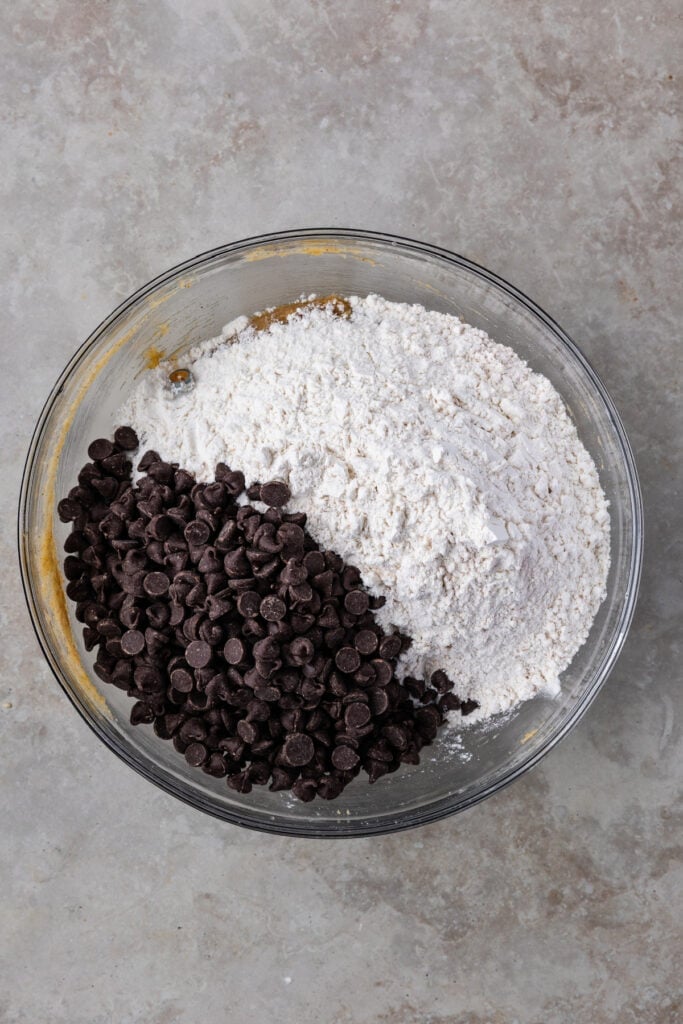 Flour and chocolate chips added to the bowl of wet ingredients, ready to be combined.