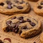 Square image of a single cookie with melted chocolate and a soft, chewy center on parchment.