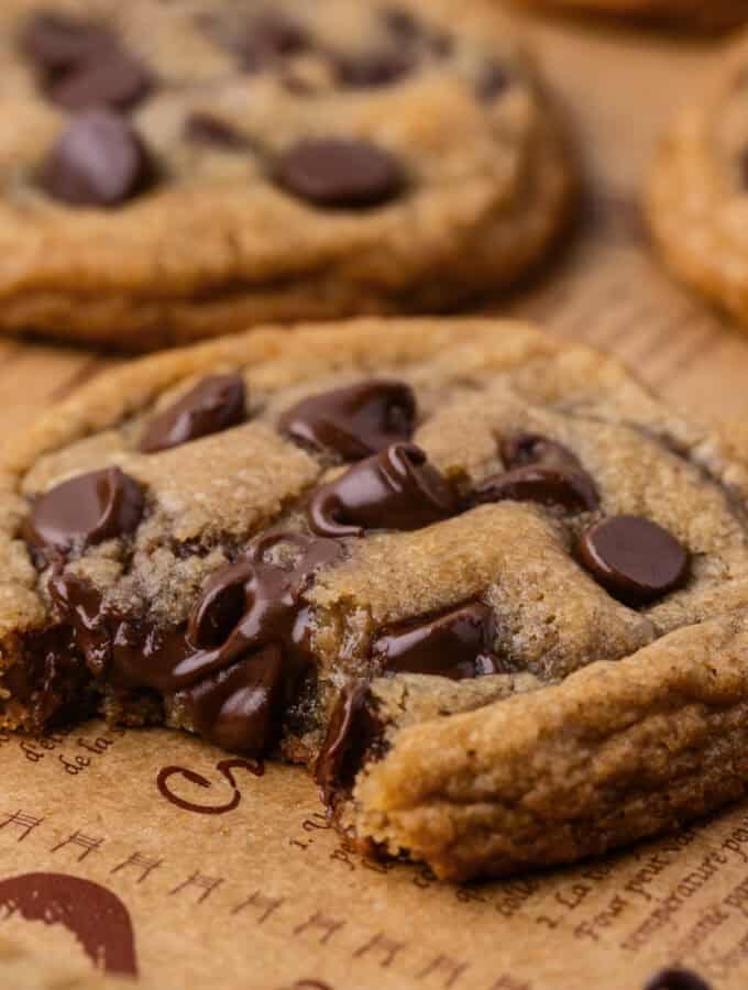 Square image of a single cookie with melted chocolate and a soft, chewy center on parchment.