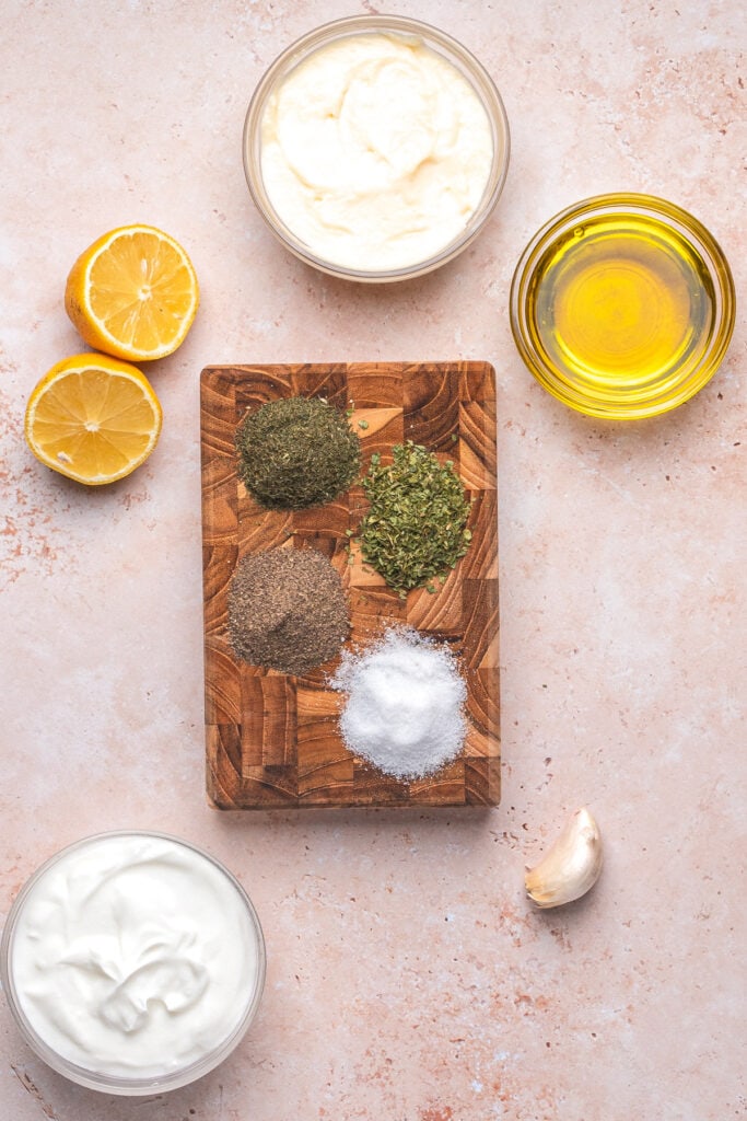 Ingredients for creamy lemon dill dressing laid out, including herbs, lemon, garlic, and dairy.