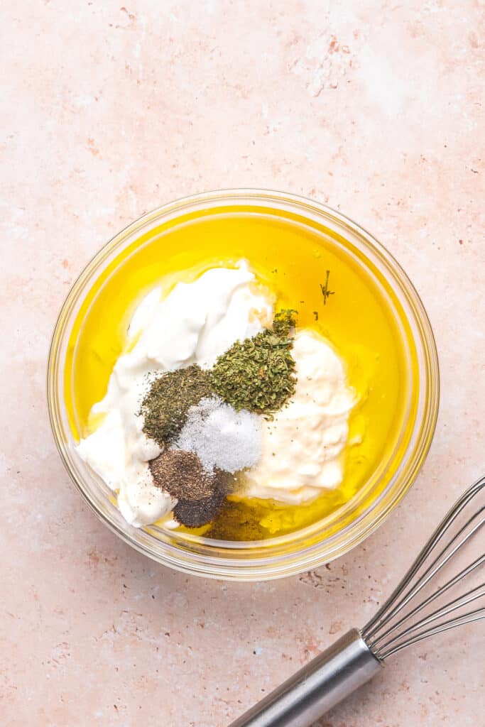 All dressing ingredients added to a glass mixing bowl, ready to be whisked together.