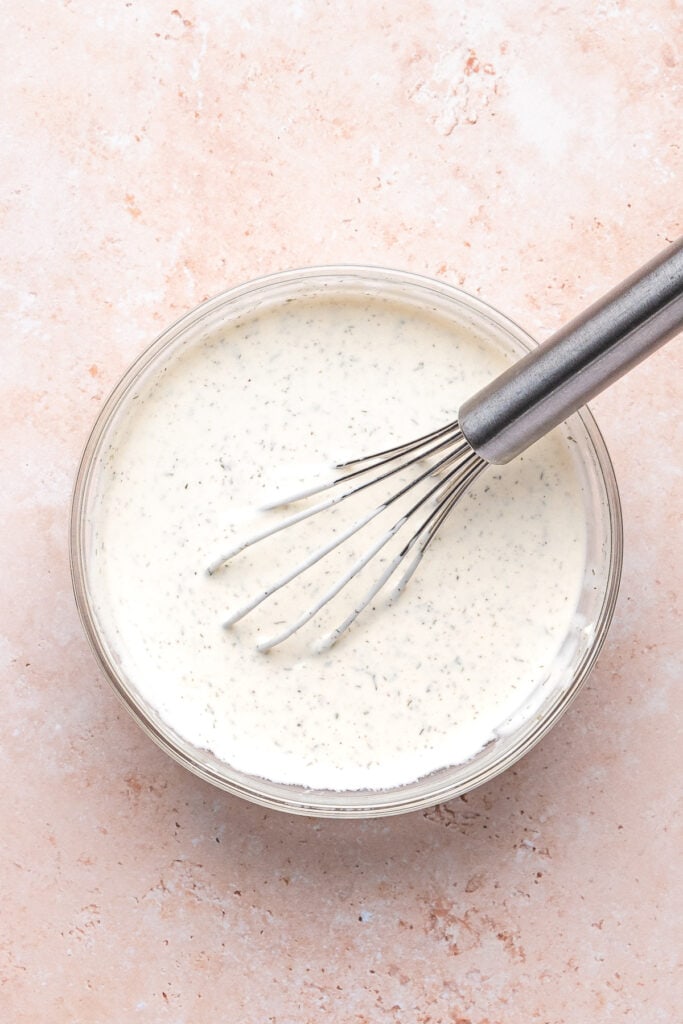 Whisking the creamy lemon dill dressing mixture until smooth and blended.