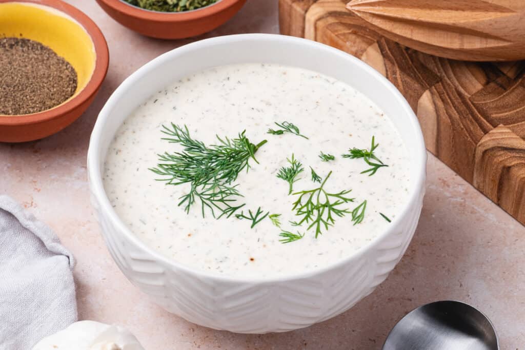 Side view of lemon dill dressing in a white textured bowl with dill garnish.
