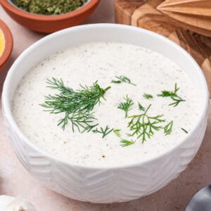 Square image of creamy lemon dill dressing in a bowl topped with fresh dill.