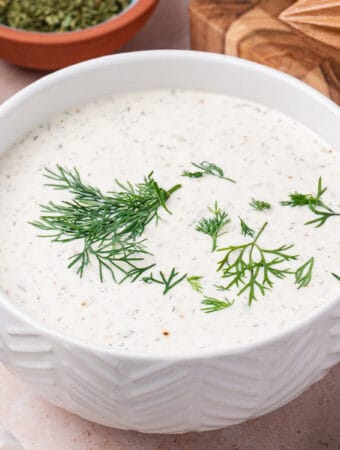 Square image of creamy lemon dill dressing in a bowl topped with fresh dill.