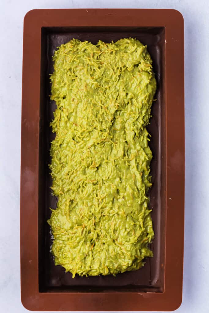 Filled chocolate bar mold with the green pistachio-kataifi-tahini mixture spread in the center.