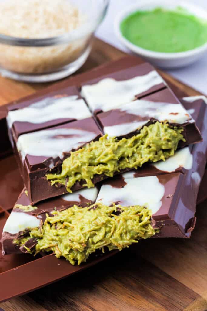 Close-up side view of two stacked Dubai Chocolate Bar pieces, filled with green pistachio-kataifi mixture and drizzled with white chocolate.