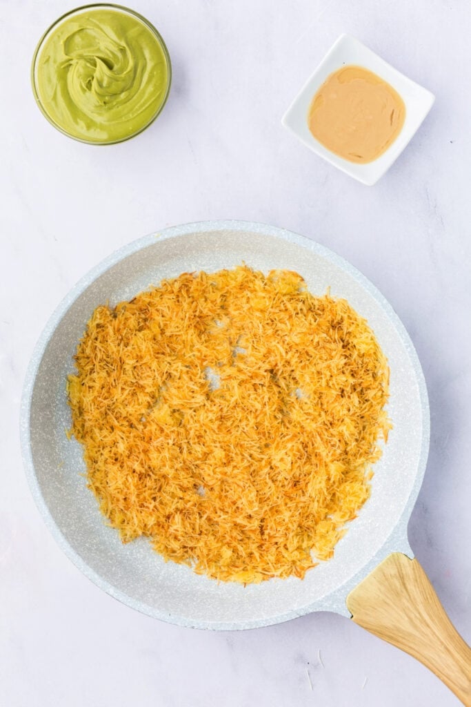 Golden, toasted kataifi pastry spread evenly in a skillet, with bowls of pistachio butter and tahini nearby.