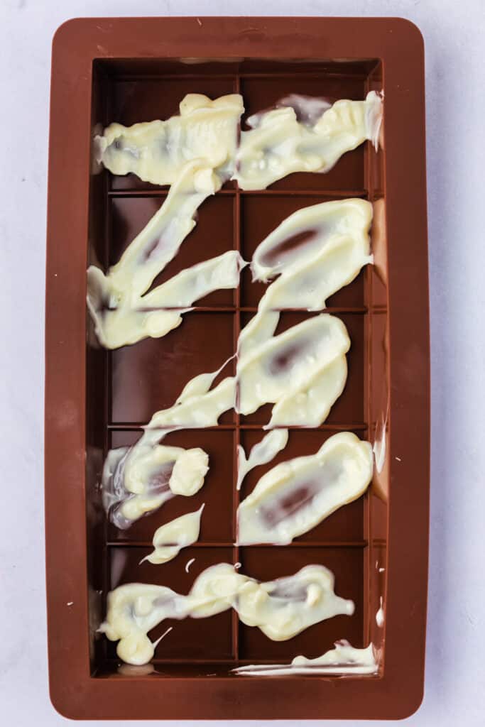 ilicone chocolate bar mold with white melting candy drizzled in a decorative pattern.