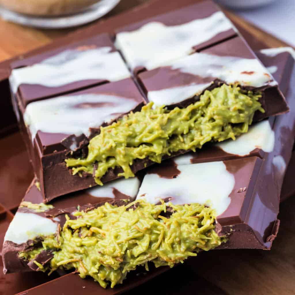 Square crop of two Dubai Chocolate Bars stacked on top of each other with visible green pistachio filling and white chocolate drizzle.