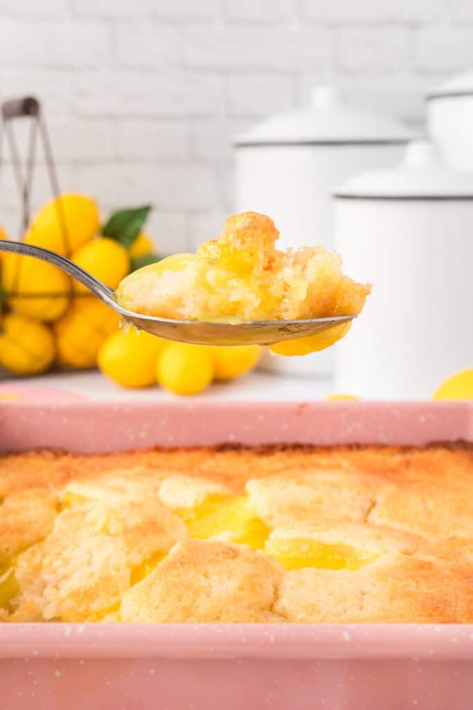 Spoonful of warm Easy Lemon Cobbler lifted from the dish showing golden topping and lemon filling
