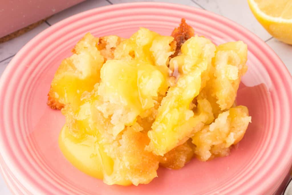 Close-up of a serving of Easy Lemon Cobbler on a pink plate, showing golden crust and lemon filling