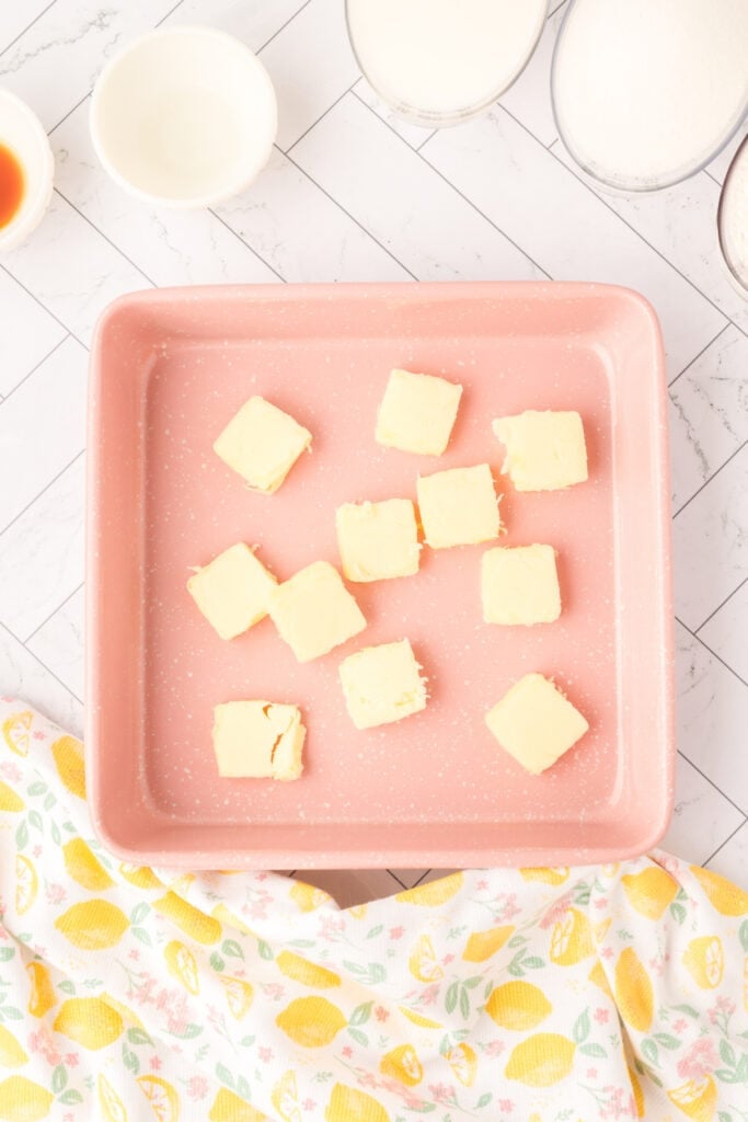 Cubes of butter arranged in a pink baking dish, ready to melt in the oven
