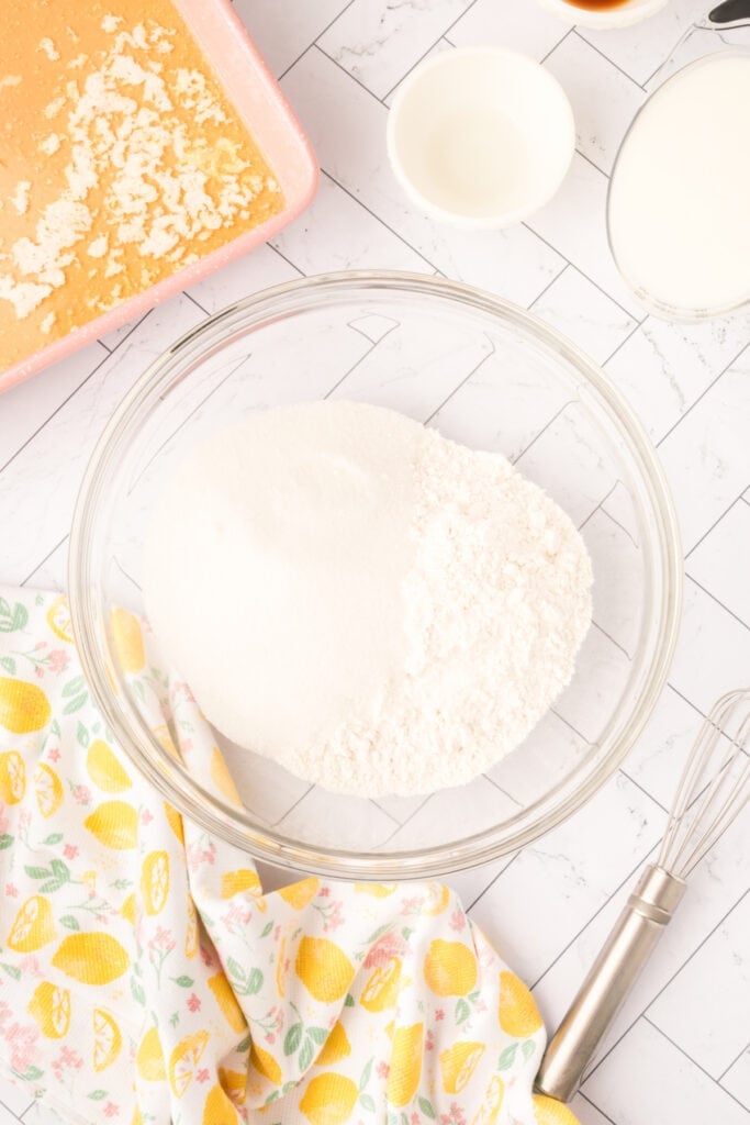Flour and sugar combined in a glass bowl beside the baking dish