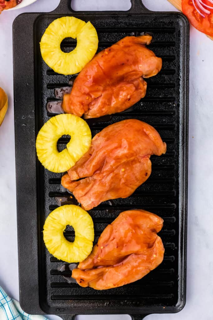 Marinated chicken breasts and pineapple slices grilling on a stovetop grill pan.