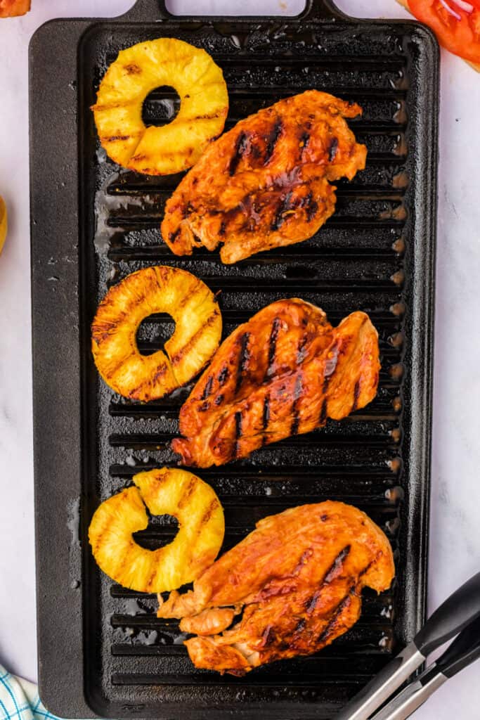 Grilled chicken breasts and pineapple slices with visible char marks on a grill pan.