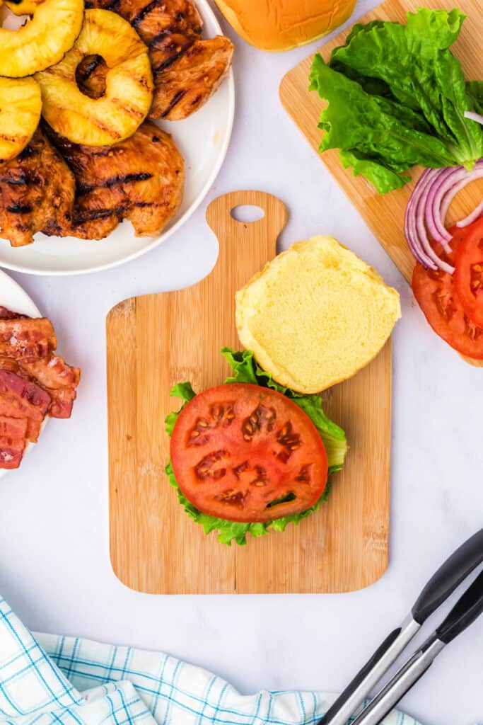 Assembling the sandwich starting with lettuce and tomato layered on the bottom bun.