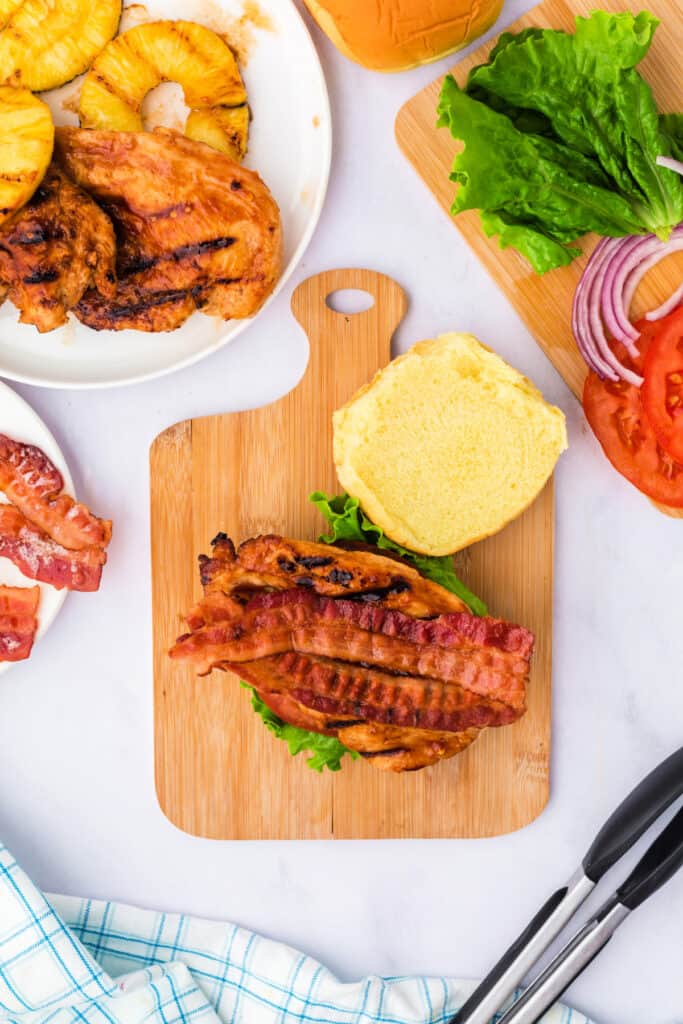Adding crispy bacon strips over the grilled chicken on the sandwich.