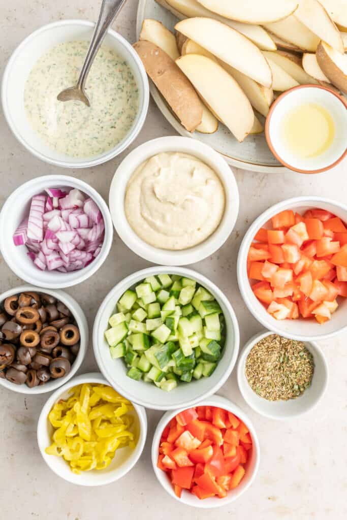 Overhead view of small bowls with toppings and sauces arranged around a plate of raw potato wedges.